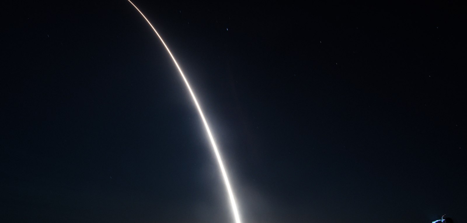 Long-exposure photograph of a missile arcing across a dark night sky against stars